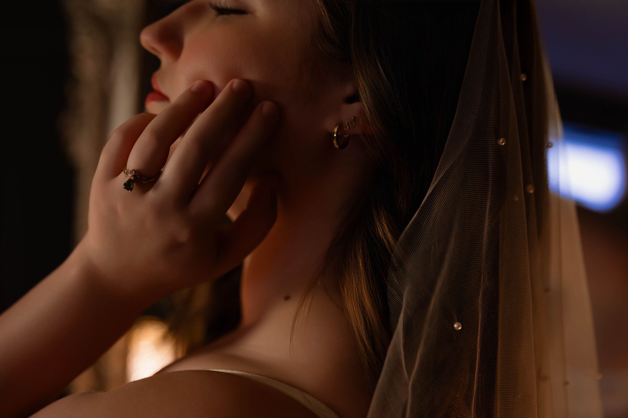 Close-up bridal boudoir portrait of Chloe touching her face beneath a soft veil, captured in warm golden light by Purdy K Photo in Cottage Grove, Oregon.